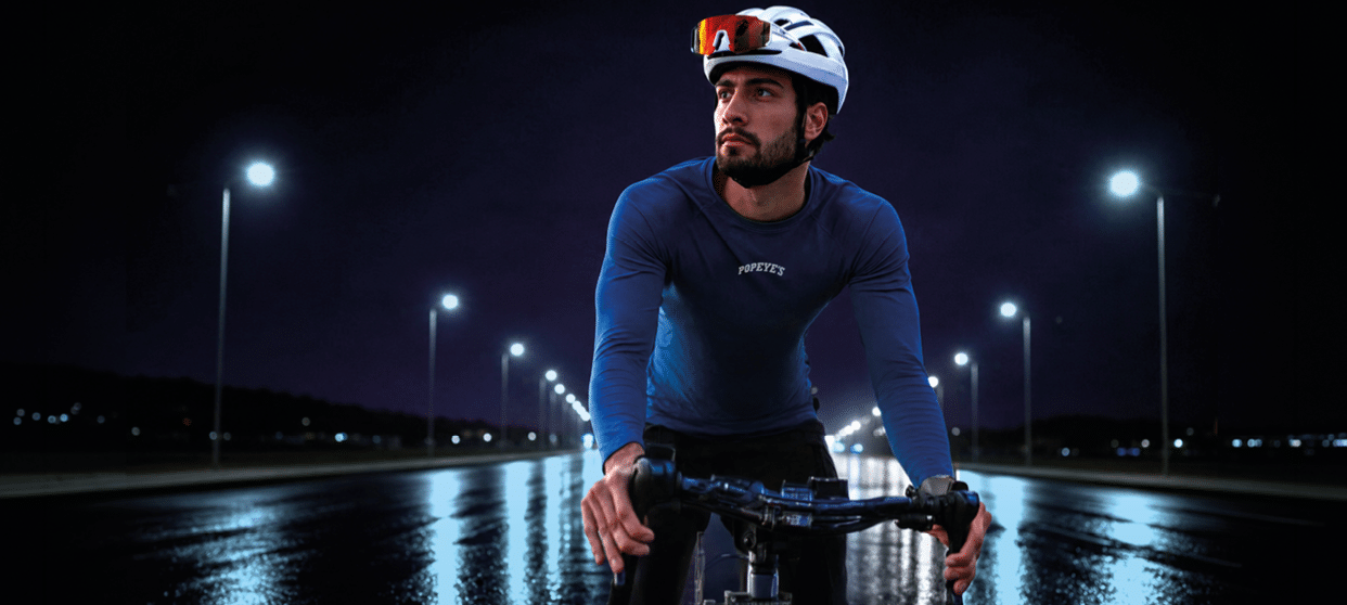 A person wearing a helmet and a long-sleeve shirt is sitting on a bicycle on a wet road at night with streetlights illuminating the scene. Description generated by AI